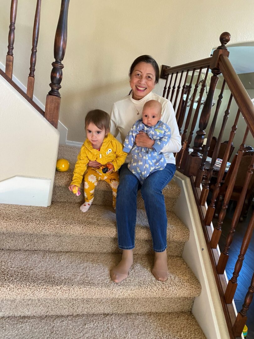 An older woman sitting on the stairs with two young kids