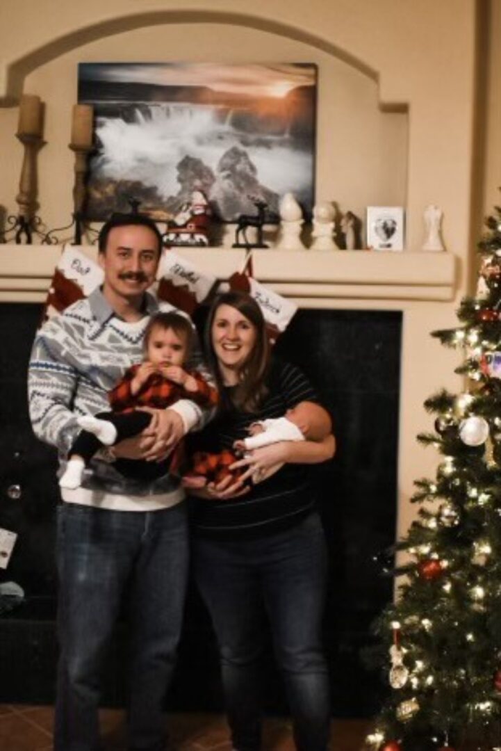 A couple holding two young children next to a Christmas tree